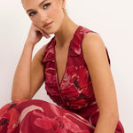 A woman wearing a sleeveless deep V-neck dress with a red and pink floral pattern, posing against a plain white background.