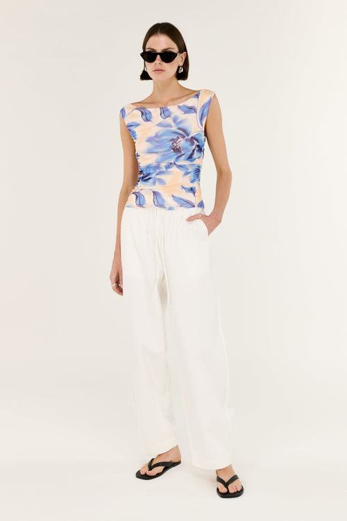 Woman wearing a floral sleeveless top and white pants on a white background