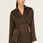 Woman wearing a brown blouse with a peplum waist on a white background