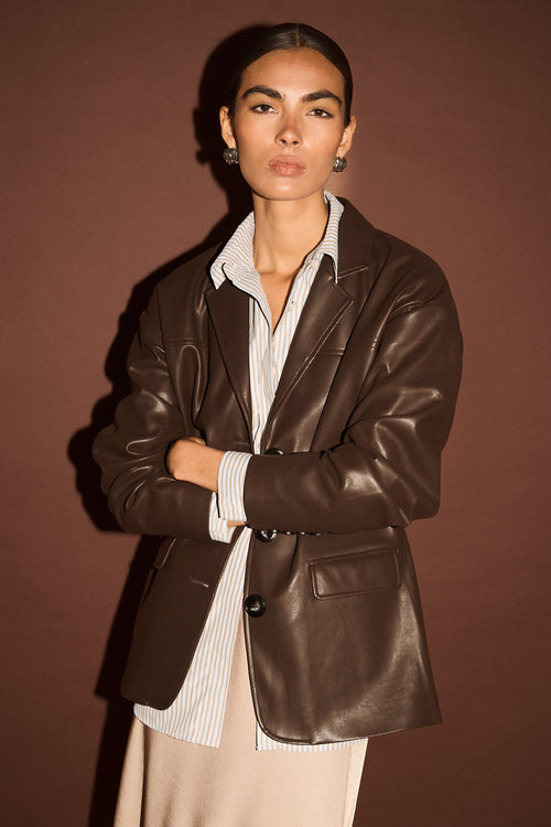 Woman wearing a brown leather jacket over a white shirt with a brown background