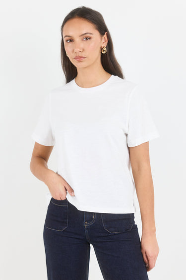 A woman modeling a plain white short-sleeve crewneck t-shirt paired with dark blue jeans, photographed against a clean white studio background.