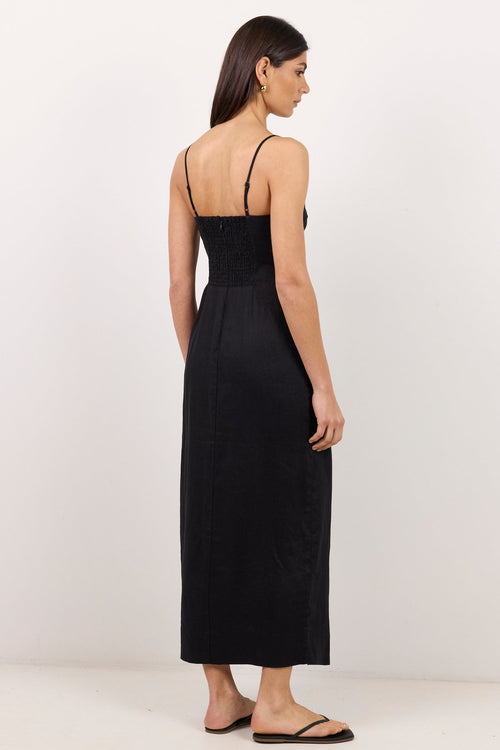 A woman modeling a black midi-length spaghetti-strap dress from the back, standing against a plain white studio background.