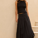 Woman in a black outfit standing on a staircase against a beige wall