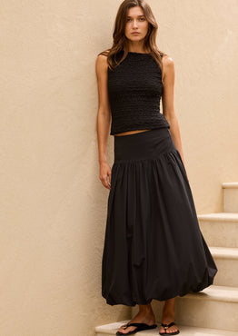 Woman in a black outfit standing on a staircase against a beige wall
