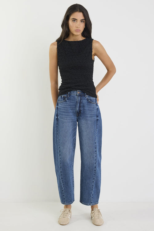 Woman wearing a black sleeveless top and blue jeans on a white background