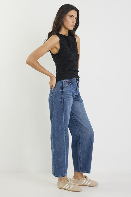 Woman wearing a black sleeveless top and blue jeans on a white background