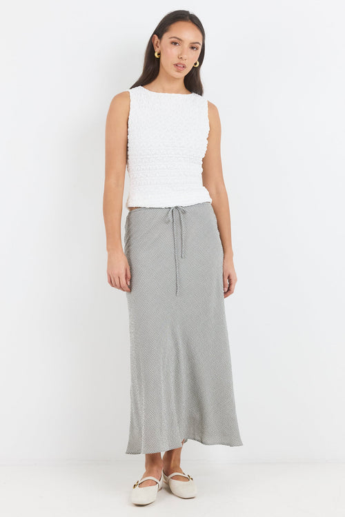 Woman wearing a white sleeveless top and gray skirt on a white background