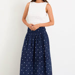 Woman wearing a white top and navy skirt with white patterns on a white background