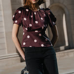 Woman in a polka dot top standing next to a lamp post with classical architecture in the background