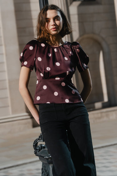 Woman in a polka dot top standing next to a lamp post with classical architecture in the background