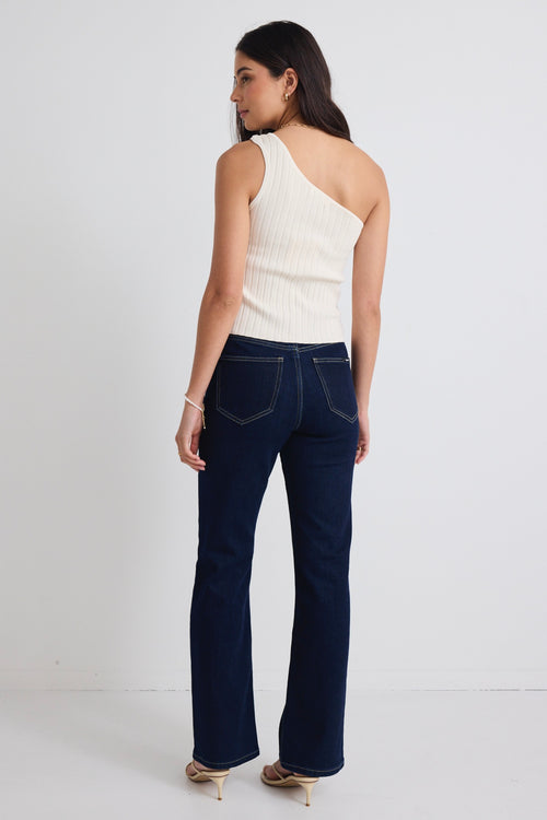 model wears dark blue jeans and one shoulder cream tp with beige heels