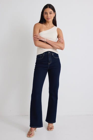 model wears dark blue jeans and one shoulder cream tp with beige heels