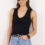 A woman modeling a black ribbed tank top and light-wash blue jeans against a plain white background.