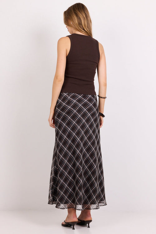 A woman shown from the back wearing a sleeveless dark brown top and a long black skirt with a white geometric grid pattern, standing against a plain white studio background.