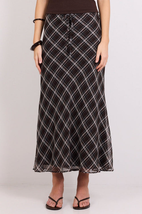 A woman modeling a dark brown sleeveless tank top and a black maxi skirt with a white diagonal grid pattern, standing against a plain white studio background.