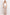 A woman stands against a plain white studio background wearing a white sleeveless top, light beige wide-leg trousers, and dark sandals.