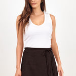 A woman modeling a white sleeveless tank top and a dark brown wrap-style mini skirt with a tie waist, photographed against a plain light background.