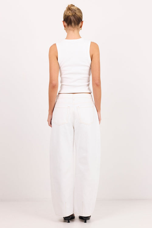 A woman viewed from behind wearing a white sleeveless crop top and white wide-leg jeans, standing against a plain white studio background.