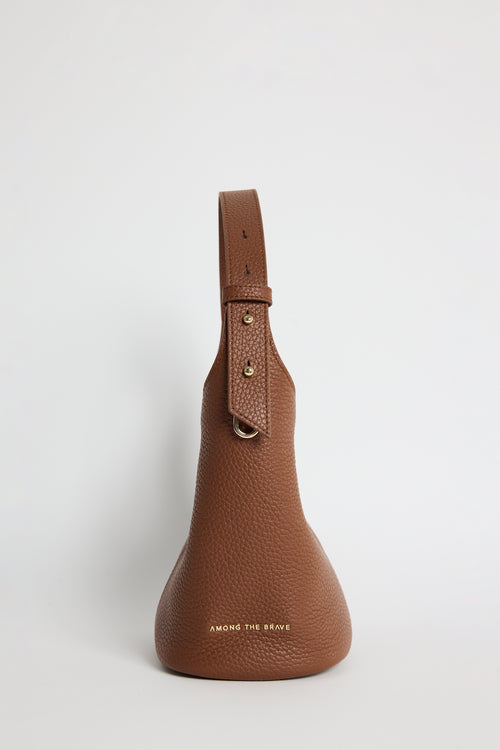 A brown pebbled leather shoulder bag with a structured teardrop silhouette, a single top handle, and gold-tone hardware, photographed against a clean light gray background.