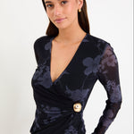 Model wearing a long-sleeve midnight floral mesh crossover top with gathered waist detail and gold hardware.