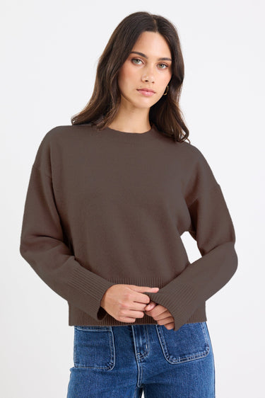 Woman wearing a brown sweater and blue jeans on a white background