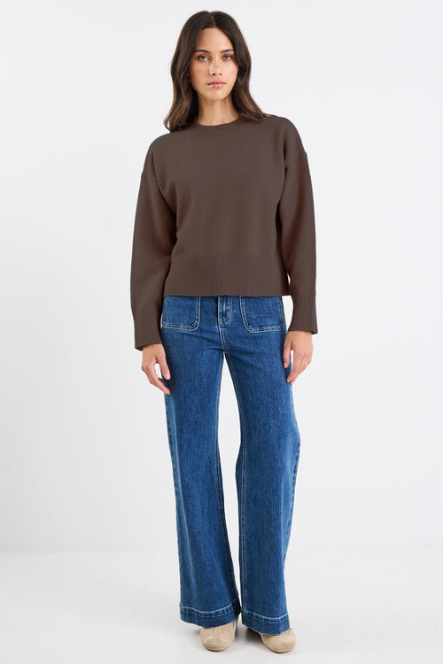 Woman wearing a brown sweater and blue jeans on a white background
