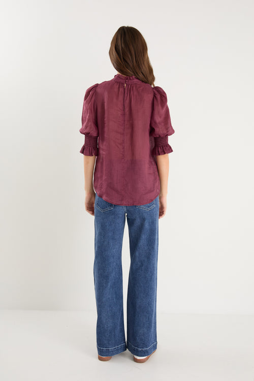 Person wearing a burgundy blouse and blue jeans on a white background