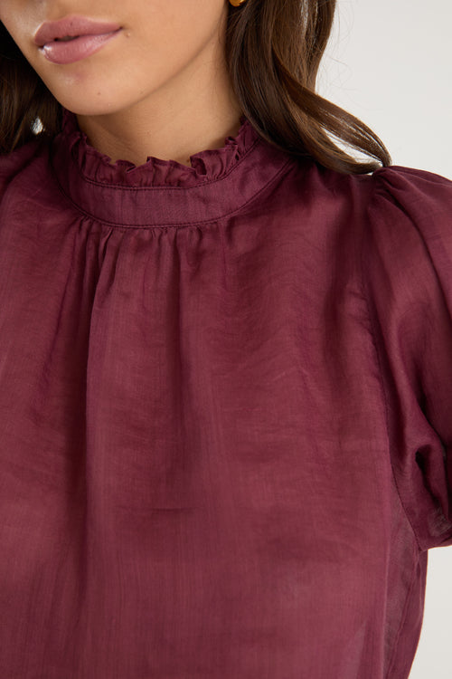 Close-up of a person wearing a burgundy blouse with puffed sleeves on a white background