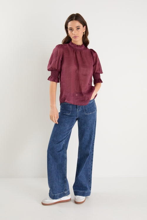Woman wearing a burgundy blouse and blue jeans on a white background