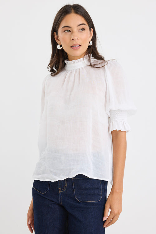 woman wearing a relaxed ivory short sleeve top with frilled neckline and sleeves, paired with indigo jeans.