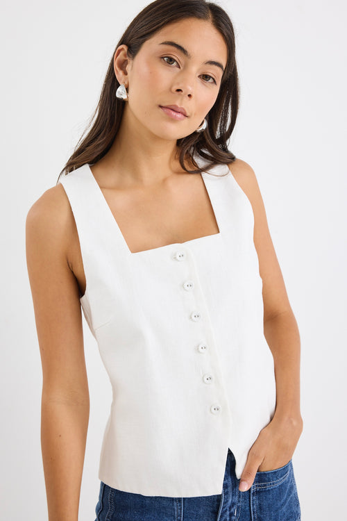 Woman wearing an ivory sleeveless linen vest with an off-centre button-down front, styled with blue jeans.