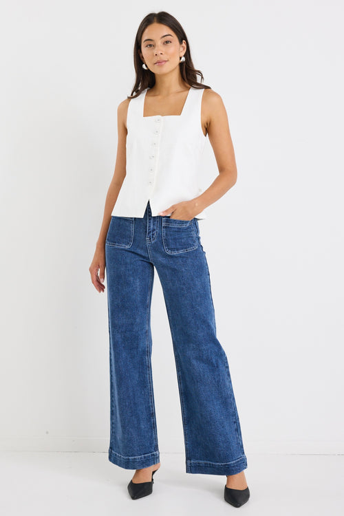 Woman wearing an ivory sleeveless linen vest with an button-down front, styled with blue jeans.