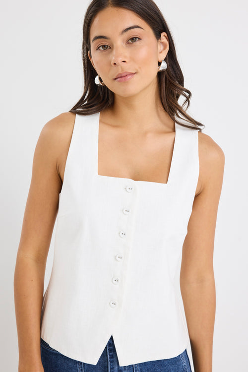 Woman wearing an ivory sleeveless linen vest with an button-down front, styled with blue jeans.