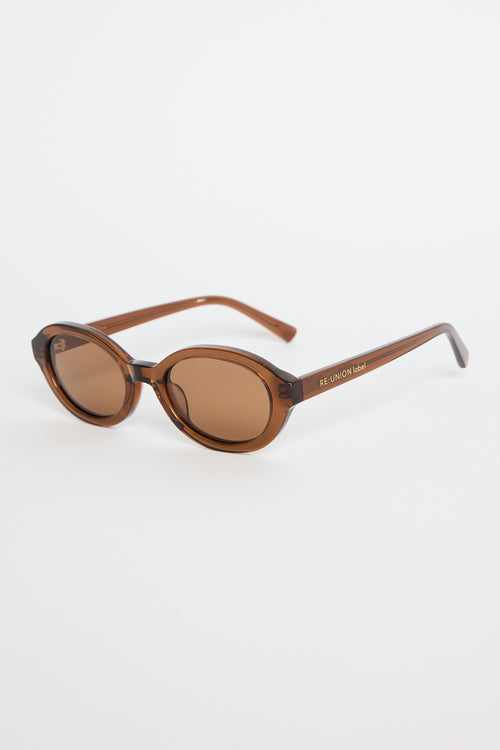 Espresso-brown oval sunglasses with tinted lenses and slim arms featuring RE:UNION label branding, photographed on a white background
