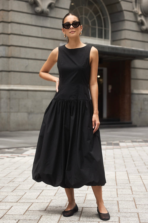 Woman wearing a black bubble hem midi dress, styled with black flats for a playful yet sophisticated look.