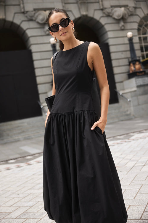 Woman wearing a black bubble hem midi dress, styled with black flats for a playful yet sophisticated look.