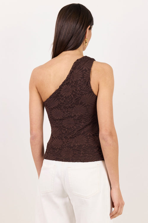 A woman shown from the back wearing a dark brown one-shoulder lace top and white pants, photographed against a plain light background.