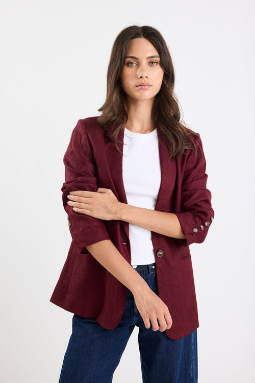 Woman wearing a burgundy blazer over a white shirt and blue jeans on a white background