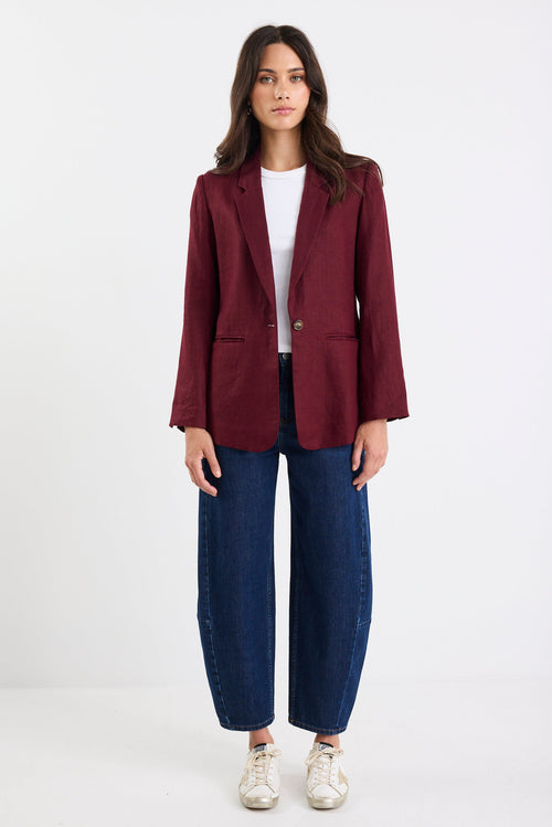 Woman wearing a burgundy blazer, white shirt, and blue jeans on a white background