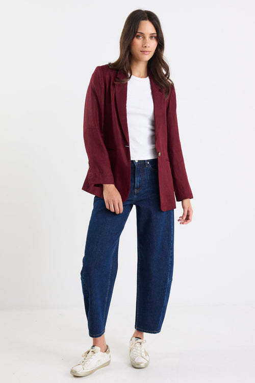 Woman wearing a burgundy jacket, white shirt, blue jeans, and white sneakers on a white background