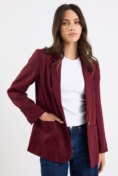 Woman wearing a burgundy blazer over a white shirt and blue jeans on a white background