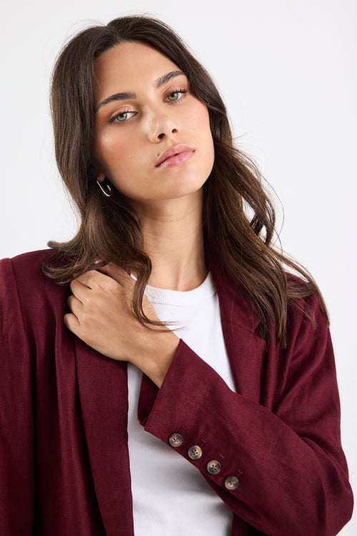 Woman wearing a burgundy blazer over a white shirt on a plain background