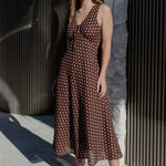 Woman in a brown polka dot dress standing against a textured wall.
