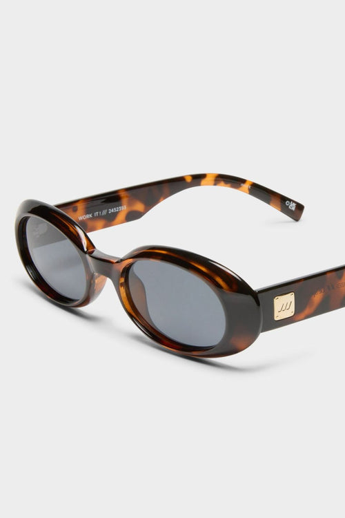 Front-facing view of oval sunglasses in a glossy dark tortoiseshell frame with smoke-tinted polarised lenses. The compact, rounded silhouette nods to 90s retro styling, offering a bold yet wearable look.