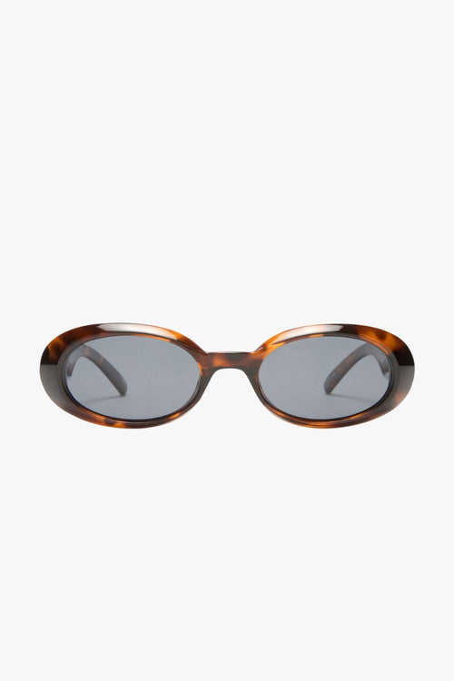 Front-facing view of oval sunglasses in a glossy dark tortoiseshell frame with smoke-tinted polarised lenses. The compact, rounded silhouette nods to 90s retro styling, offering a bold yet wearable look.