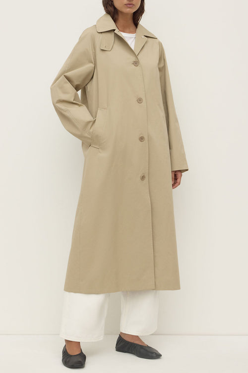 Person wearing a beige trench coat on a white background
