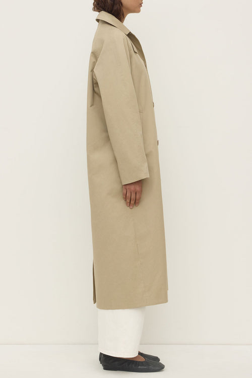Person wearing a beige trench coat on a white background