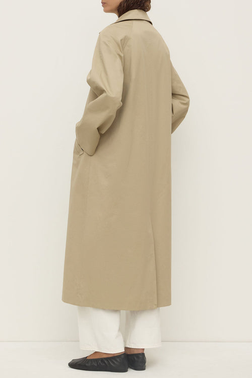 Person wearing a beige trench coat on a white background