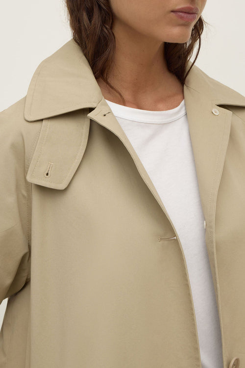 Beige trench coat worn by a person on a plain background