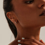 Model wears wavey rhodium hoop earring.